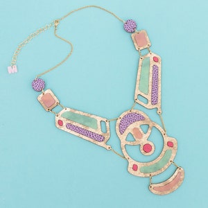 Peut inclure: Un collier en or avec un design géométrique orné d'accents roses, verts et violets. Le collier est en cuir et en métal.