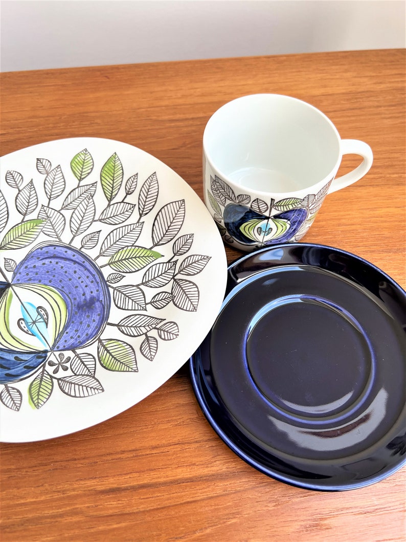 以下が含まれることがあります： 青と緑の花柄が描かれた白い陶磁器のティーカップとソーサー。ソーサーは濃い青一色です。