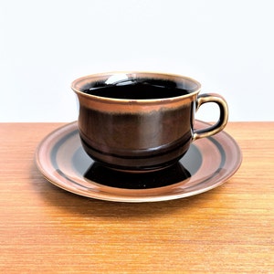Puede incluir: Una taza de té y un platillo de cerámica marrón y negro con un diseño a rayas. La taza está llena de té negro.