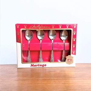 以下が含まれることがあります： 金色の文字で「Hilzjohann」と「Maringo」と書かれた赤い箱に入った、銀製のティースプーン4本セットです。