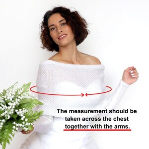 May include: A white off-the-shoulder knitted shrug with long sleeves. The measurement should be taken across the chest together with the arms.