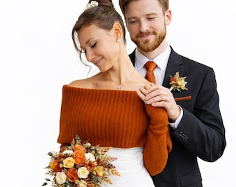 May include: A rust-colored off-the-shoulder ribbed knit bolero worn over a white dress, paired with a black suit featuring a rust-colored tie and pocket square, and a bouquet of orange, white, and yellow flowers with green foliage.
