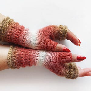 Puede incluir: Un par de guantes sin dedos tejidos a mano en tonos rojos, blancos y marrones. Los guantes presentan un diseño texturizado con detalles calados y están diseñados para cubrir la mano hasta los nudillos.
