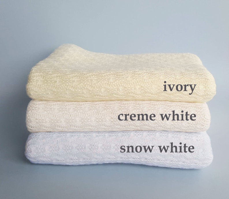 May include: A stack of three folded knitted blankets featuring a textured cable pattern. The top blanket is labeled ivory, the middle blanket is labeled creme white, and the bottom blanket is labeled snow white, with each color name printed next to it.