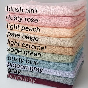 May include: A stack of folded knit blankets featuring a delicate openwork pattern. The colors are labeled as blush pink, dusty rose, light peach, pale beige, light caramel, sage green, dusty blue, pigeon gray, gray, and burgundy.