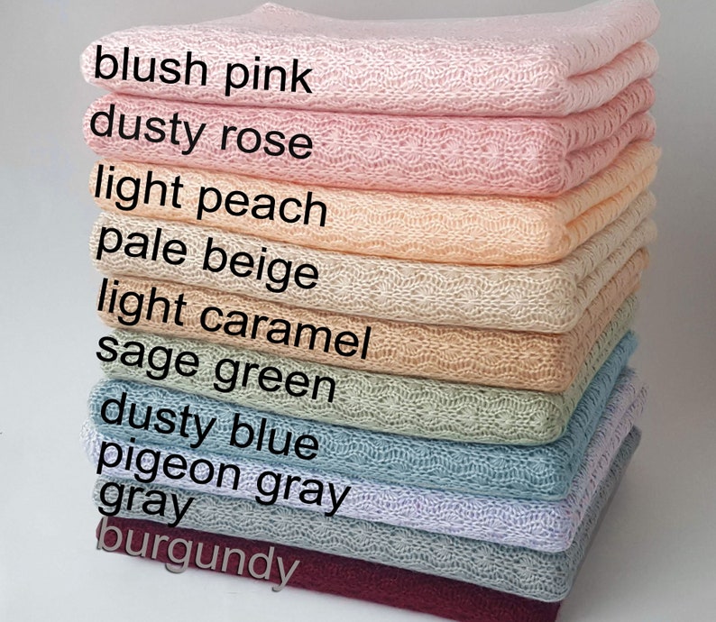 May include: A stack of folded knit blankets featuring a delicate openwork pattern. The colors are labeled as blush pink, dusty rose, light peach, pale beige, light caramel, sage green, dusty blue, pigeon gray, gray, and burgundy.