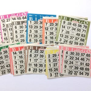 May include: A collection of colorful paper bingo cards featuring a five-by-five grid of numbers, the word BINGO printed at the top, and a central free space. The cards are printed in various colors including pink, blue, orange, green, and yellow.