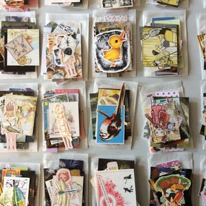 May include: A collection of vintage ephemera, including stickers and paper cutouts, arranged in small, clear packets. The assortment features illustrations of birds, cartoon characters, and other whimsical designs. The packets are neatly organized on a light-colored surface.