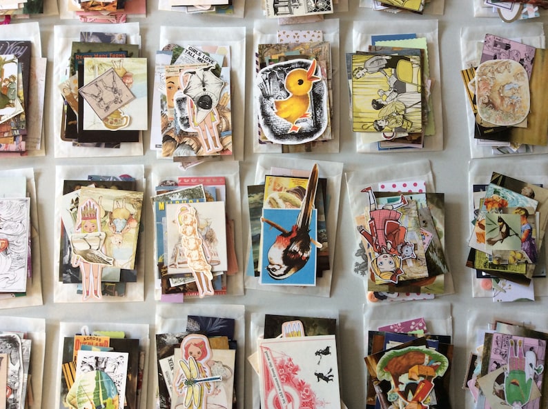 May include: A collection of vintage ephemera, including stickers and paper cutouts, arranged in small, clear packets. The assortment features illustrations of birds, cartoon characters, and other whimsical designs. The packets are neatly organized on a light-colored surface.