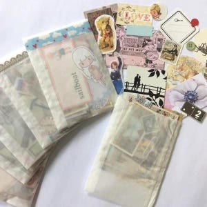 May include: A collection of vintage-style ephemera, including paper ephemera, stickers, and decorative elements. The items are arranged on a white surface, with some items in clear cellophane bags. The color palette includes soft pastels and vintage tones.
