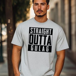 May include: A light gray t-shirt with the text "STRAIGHT OUTTA GULAG" in a black, bold font. The text is centered within a black rectangular box. The shirt is short-sleeved.
