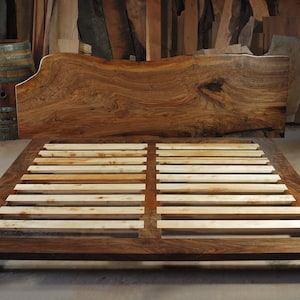 May include: A wooden bed frame with a live edge headboard and slatted base. The headboard is made of dark wood with a natural grain pattern. The base is made of lighter wood with a smooth finish.