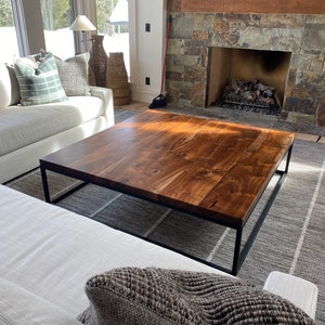 May include: A large, rectangular coffee table with a dark wood top and a black metal frame. The table is sitting on a gray and white rug in a living room.