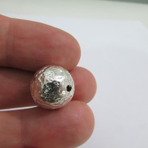 Könnte beinhalten: Eine silberne, gehämmerte Perle mit einem Loch zum Aufziehen.