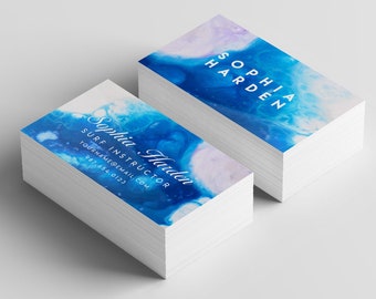 Op de afbeelding: Stapel visitekaartjes met een abstract aquarelontwerp in blauw en wit. De tekst op de kaart luidt "Sophia Harden, Surfinstructeur, yourname@email.com, 555-555-5121."
