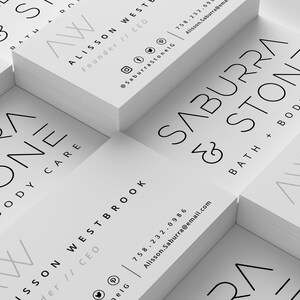 May include: A stack of white business cards with the text "Saburra & Stone Bath + Body Care" and the logo "AW" in a gray color. The text "Alisson West Founder // CEO" and contact information is also included on the cards.
