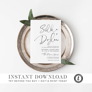 Può includere: Un invito di nozze bianco con testo in calligrafia nera che recita "Silk + Dylan" e dettagli per una cerimonia e un ricevimento di nozze. Il testo include anche la data, l'ora e il luogo del matrimonio. La carta è appoggiata su un piatto da portata argentato con foglie verdi.