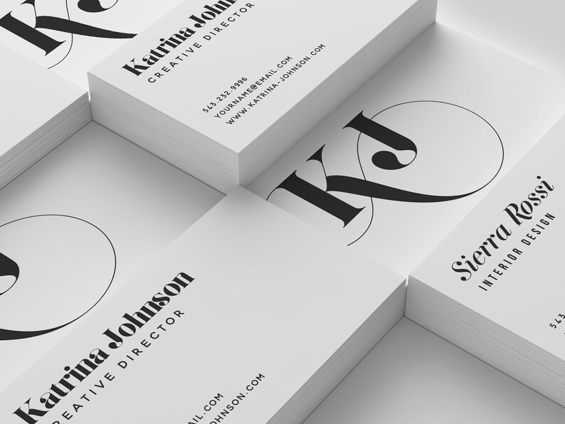 Puede incluir: Una pila de tarjetas de visita blancas con texto negro y un logotipo "KJ" estilizado. El texto de la tarjeta superior dice "Katrina Johnson, Directora Creativa". El texto de la tarjeta inferior dice "Sierra Rossi, Dise&ntilde;o de Interiores".