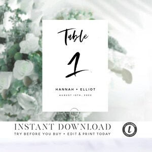 May include: White table number card with black calligraphy text that reads "Table 1" and "HANNAH + ELLIOT AUGUST 10TH, 2023".