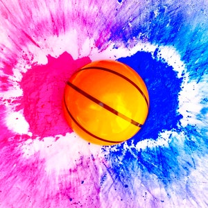 May include: A basketball with orange and black markings sits on a white surface with pink and blue powder splattered around it.