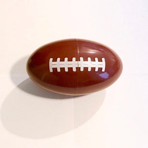 Peut inclure: Un œuf en plastique brun en forme de ballon de football avec une couture blanche.