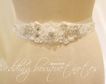 May include: White satin bridal sash with a beaded floral design featuring pearls and rhinestones. The sash is displayed on a dress form.