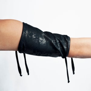 Może przedstawiać: Czarny rękaw do łokcia z fakturowanym wzorem i dwoma sznurkami na dole.