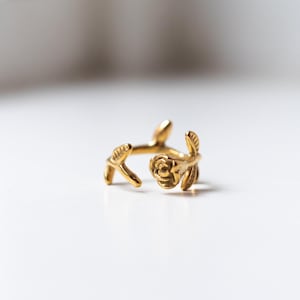 Op de afbeelding: Een gouden ring met een roos en bladeren. De ring is gemaakt van metaal en heeft een delicaat ontwerp.