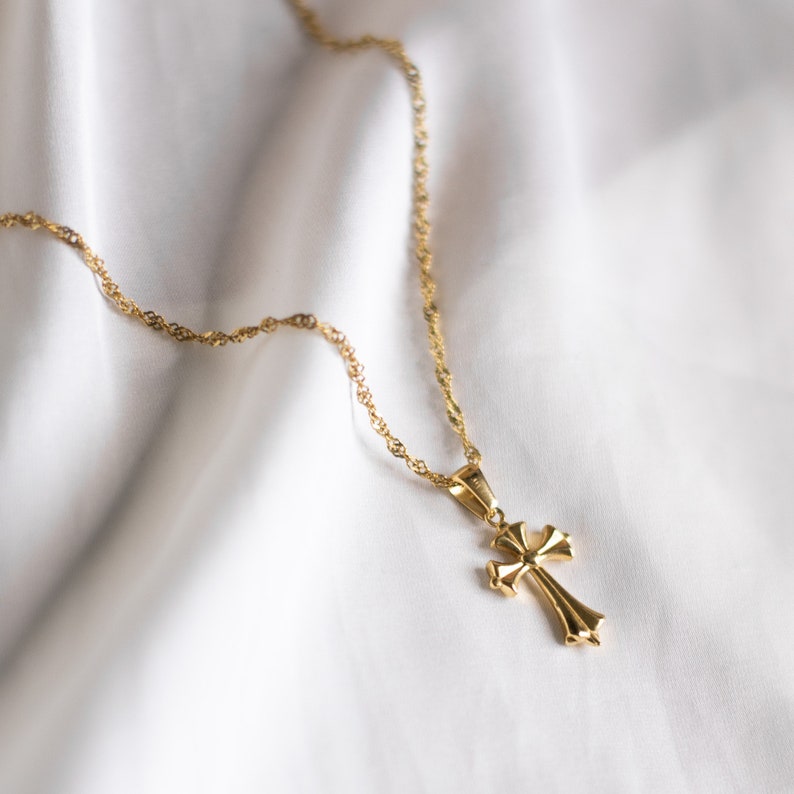 May include: A gold chain necklace with a gold cross pendant. The chain is a delicate, twisted design. The cross is a simple, classic shape.