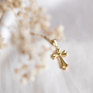 May include: A gold cross pendant necklace on a white fabric background.