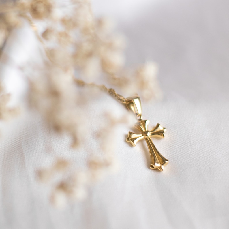 May include: A gold cross pendant necklace on a white fabric background.