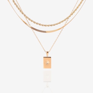 Puede incluir: Un collar de oro de capas con un colgante cuadrado que presenta un pequeño diseño de estrella.