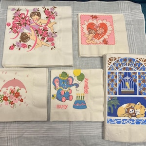 May include: A collection of vintage paper napkins with various designs. One features cherubs with pink ribbons and roses, another has cherubs inside a heart. Other napkins have an umbrella, an elephant, and a cat.