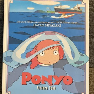 May include: A "Ponyo" picture book featuring a cartoon illustration of a girl with red hair under a blue wave. The cover includes the title "Ponyo" in red letters and the text "Picture Book". The background shows a seascape with boats.