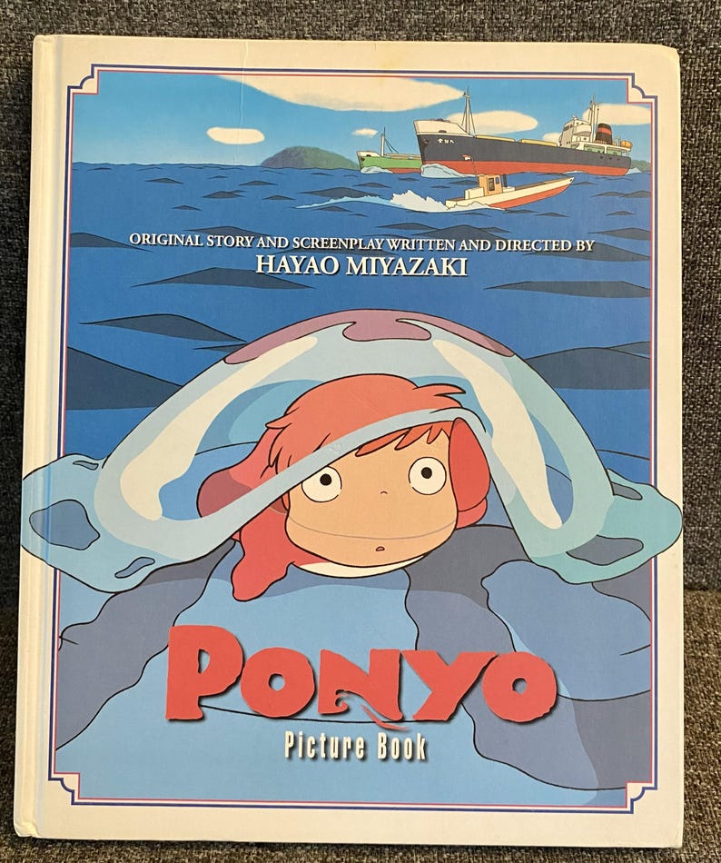 May include: A "Ponyo" picture book featuring a cartoon illustration of a girl with red hair under a blue wave. The cover includes the title "Ponyo" in red letters and the text "Picture Book". The background shows a seascape with boats.