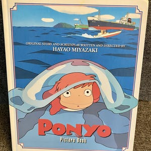 May include: A "Ponyo" picture book with a blue and white cover featuring an illustration of a character with red hair and a blue sea creature. The cover also displays the title "Ponyo" in red letters and text that reads "Original Story and Screenplay Written and Directed by Hayao Miyazaki."