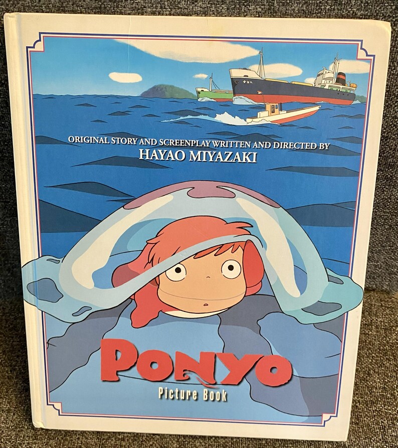 May include: A "Ponyo" picture book with a blue and white cover featuring an illustration of a character with red hair and a blue sea creature. The cover also displays the title "Ponyo" in red letters and text that reads "Original Story and Screenplay Written and Directed by Hayao Miyazaki."