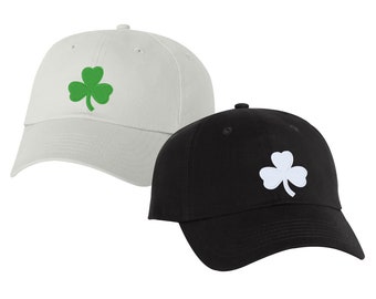 May include: Two baseball caps with an embroidered shamrock design. One cap is white with a green shamrock, and the other is black with a white shamrock.