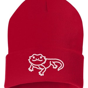 May include: Red knit beanie with a white embroidered bearded dragon design.