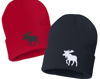 May include: Two knit beanies, one red and one navy blue, with a moose silhouette embroidered on the front. The moose on the red beanie is black, and the moose on the navy beanie is white.