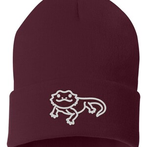 May include: A maroon beanie with a white outline of a bearded dragon on the front.