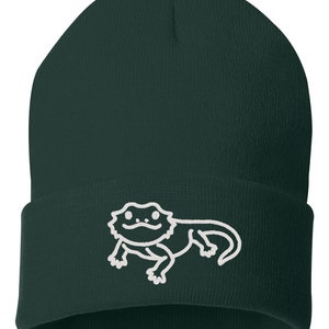 May include: A dark green beanie with a white embroidered bearded dragon design.