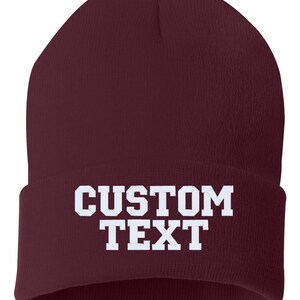 May include: A maroon beanie with the text "CUSTOM TEXT" in white.