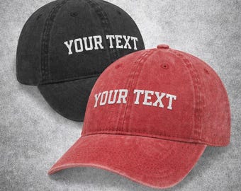 May include: Two baseball caps, one black and one red, are displayed. Each cap has the text "YOUR TEXT" in white block letters across the front. The caps are made of a textured fabric and have a classic baseball cap design.