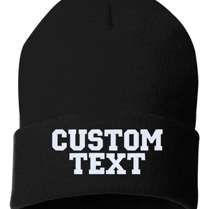 May include: Black knitted beanie with white text that reads "CUSTOM TEXT".