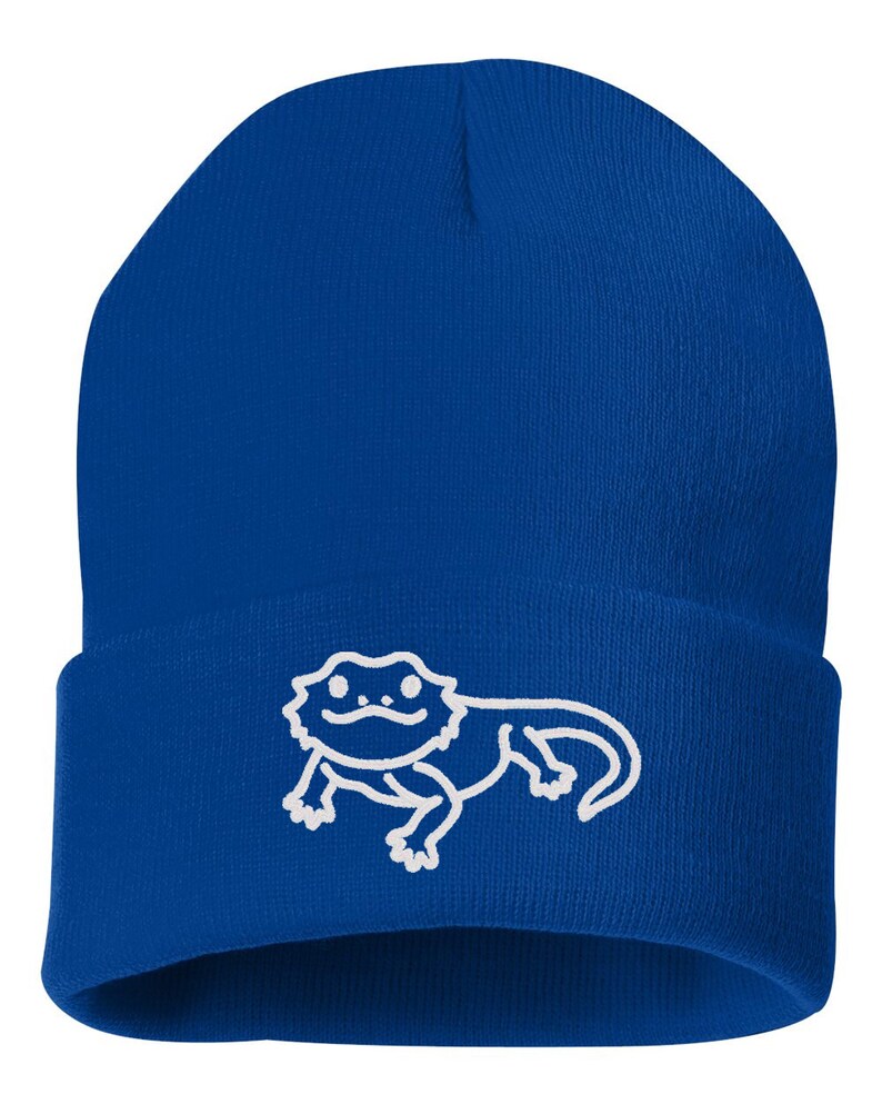 May include: A royal blue beanie with a white outline of a bearded dragon.