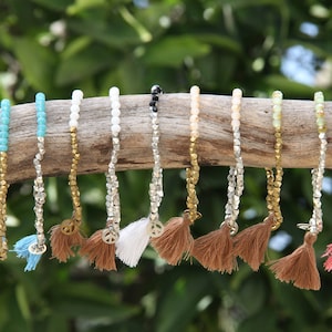 May include: A collection of 10 beaded bracelets with peace sign charms and colourful tassels. The bracelets are made with various colours of beads, including turquoise, gold, white, black, and light brown.