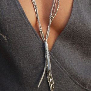 May include: A silver necklace with a long tassel pendant. The necklace is made of multiple strands of beads and leather cord.