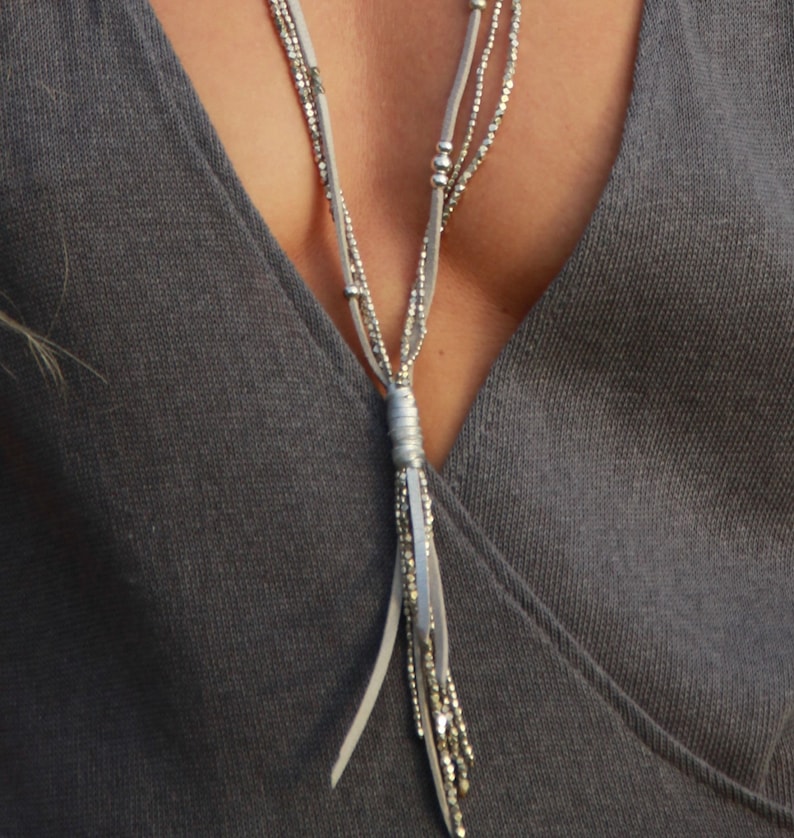 May include: A silver necklace with a long tassel pendant. The necklace is made of multiple strands of beads and leather cord.