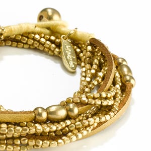 May include: A gold leather wrap bracelet with multiple strands of gold beads and a gold charm with the word "Moleskine" on it.